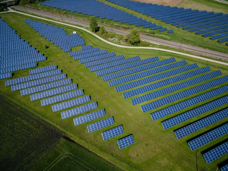 Aerial view of a ground-mounted solar park beside a railway line